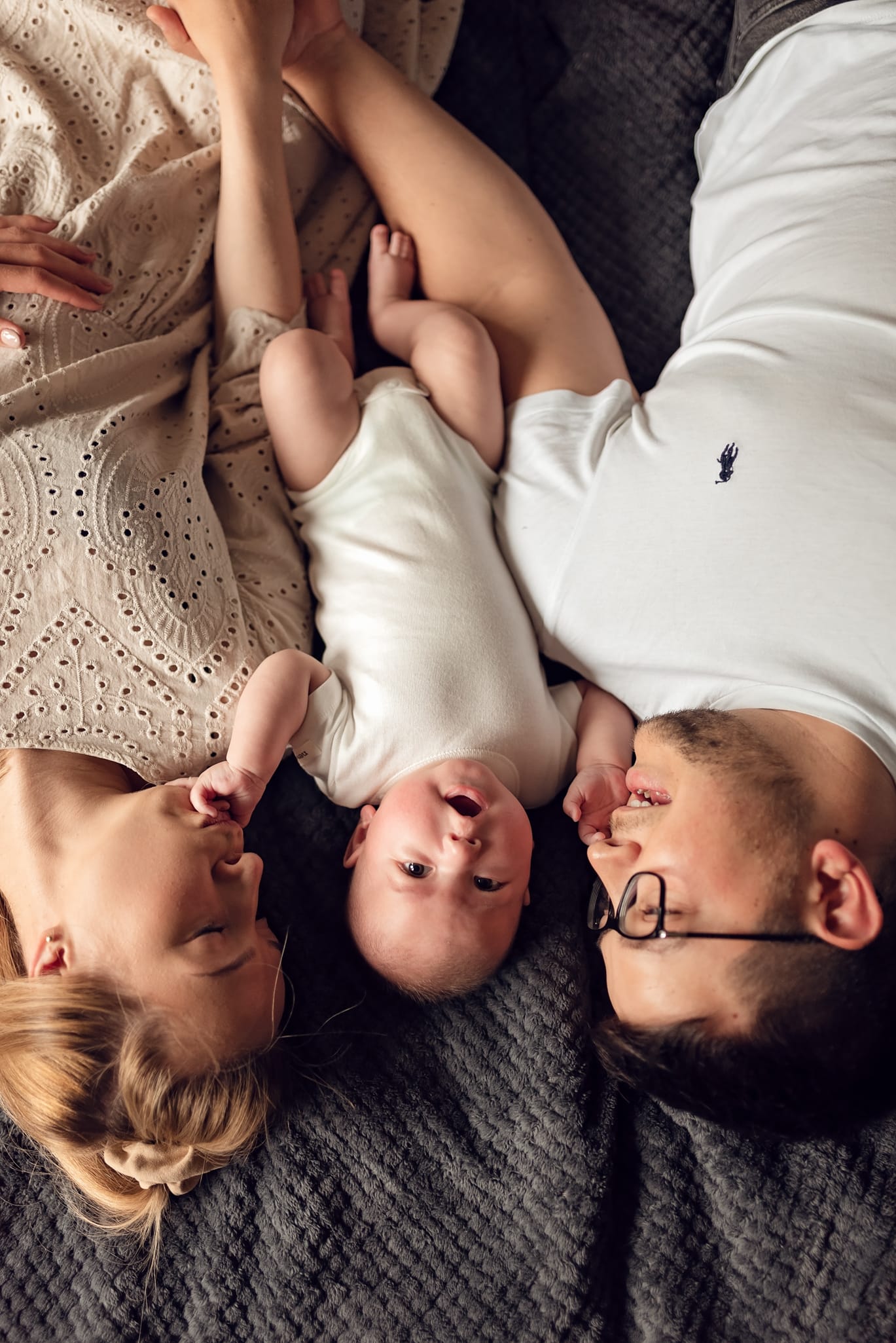 Niemowlę między rodzicami wyciąga dłonie sesja w domu