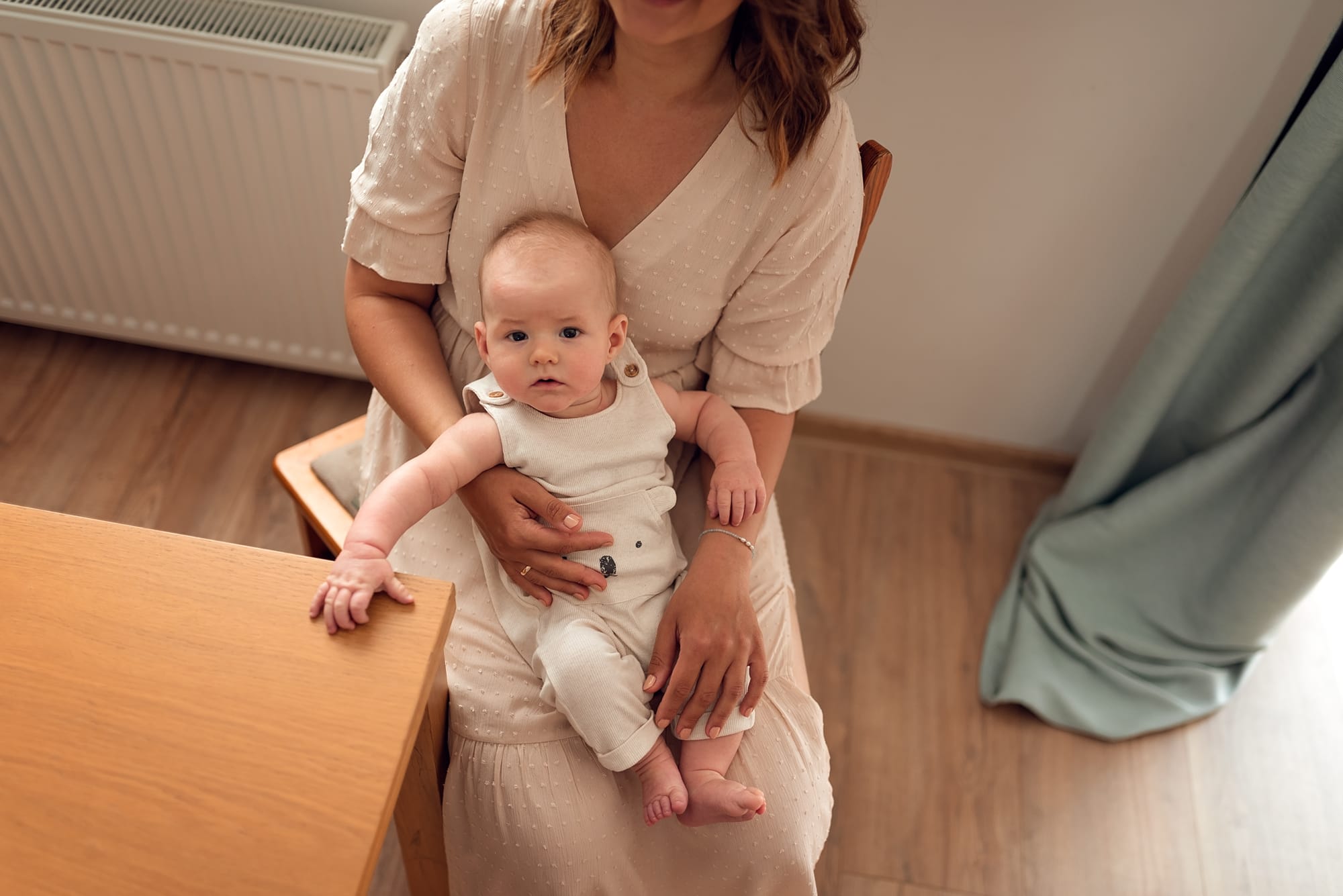 Mama z niemowlęciem, który trzyma rękę na stole sesja rodzinna w domu Gdańsk
