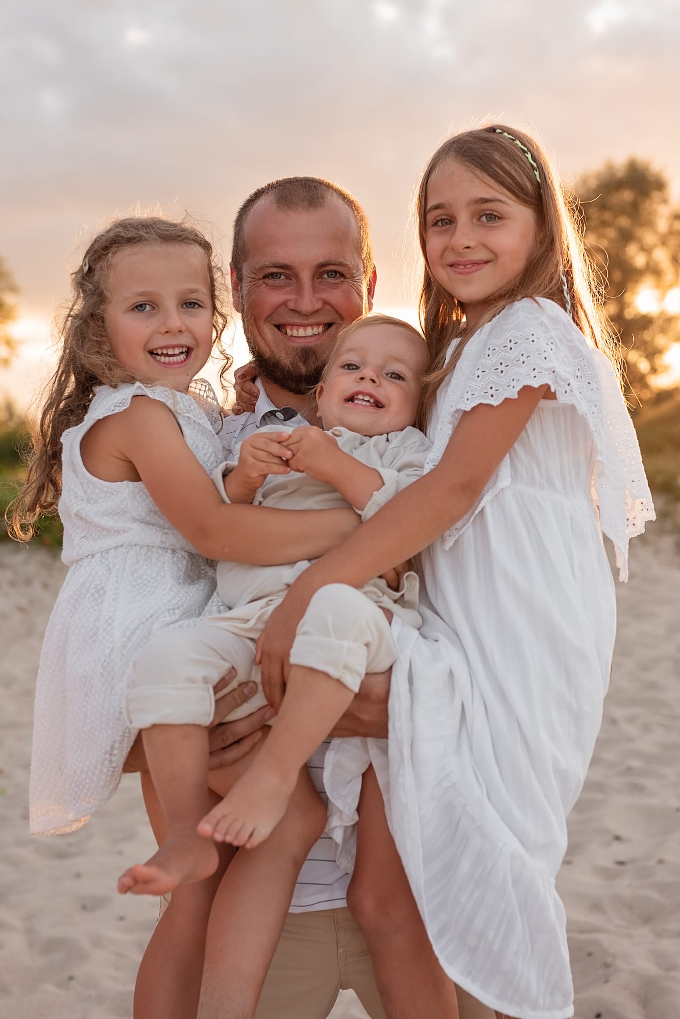 Tata trzyma trójkę dzieci na rękach sesja rodzinna plaża