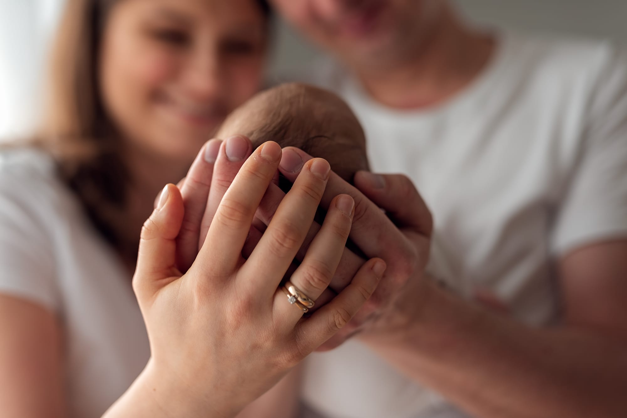 Dłonie rodziców otulają główkę noworodka sesja w domu