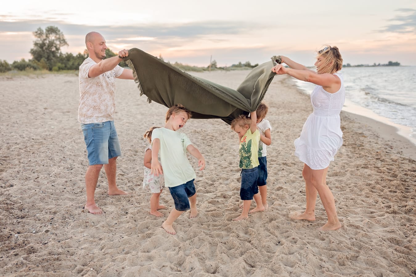 Rodzina wielodzietna zabawy z kocem na plaży