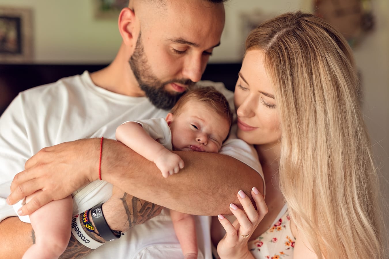 Niemowlę trzymane przez tatę w pozycji na leniwca tulone przez rodziców tworząc ciepły obrazek.