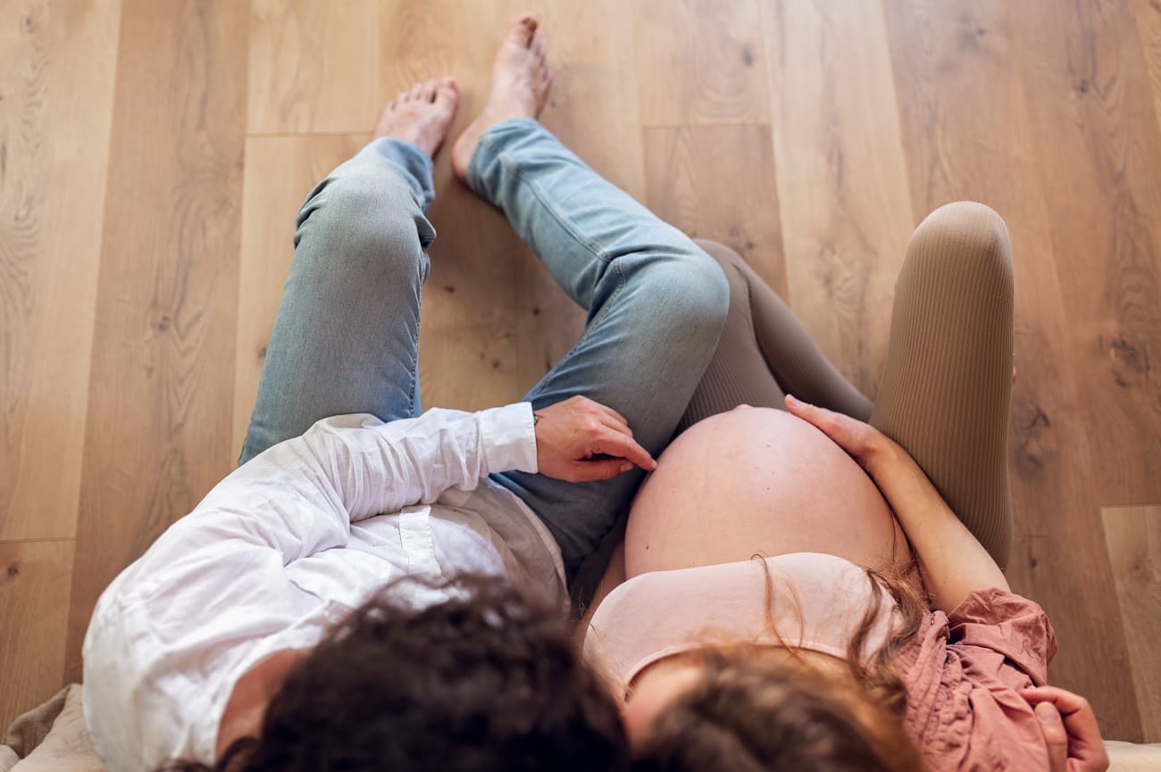 Para głaszcze brzuszek na kanapie sesja ciążowa w domu