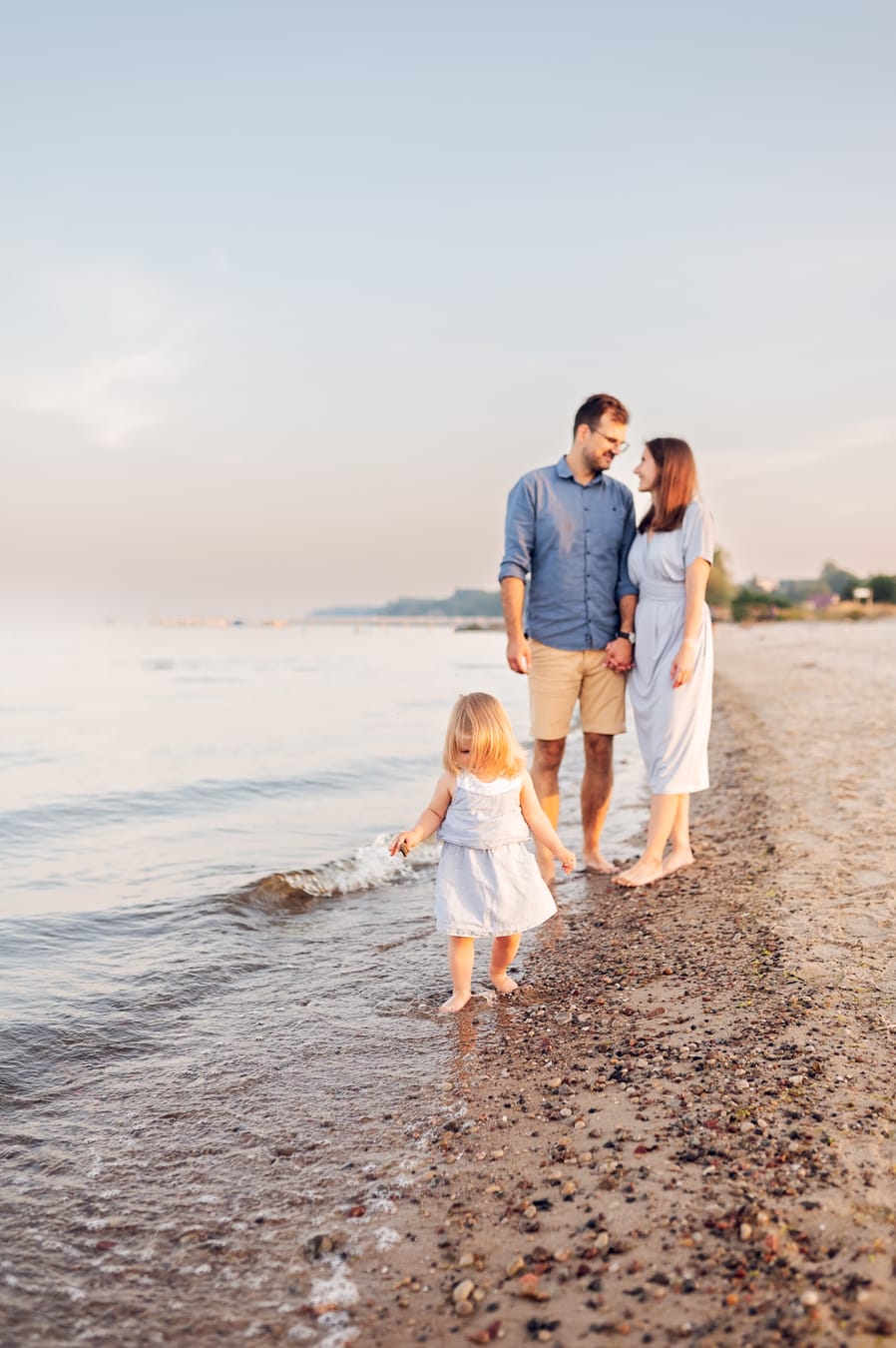 Dziewczynka zbiera kamienie rodzice w tle plaża
