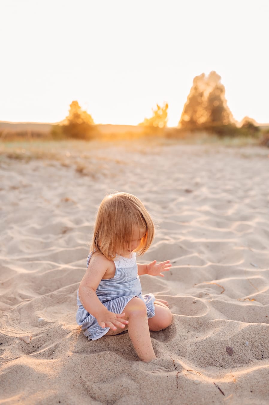 Dziewczynka zakopuje stopy w piasku sesja nad morzem