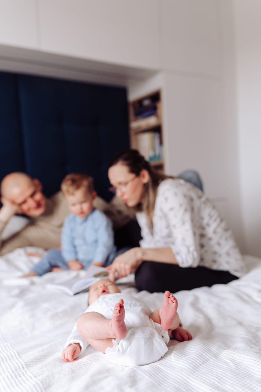 Niemowlę na łóżku rodzice czytają starszakowi sesja
