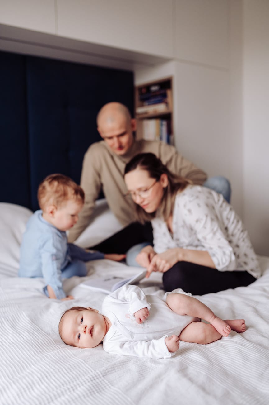 Niemowle na łóżku rodzice czytają starszakowi sesja
