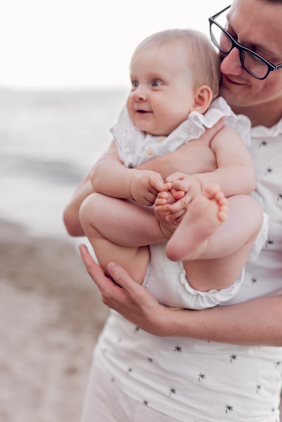 Niemowlę bawi się stópkami na rękach taty plaża Gdynia