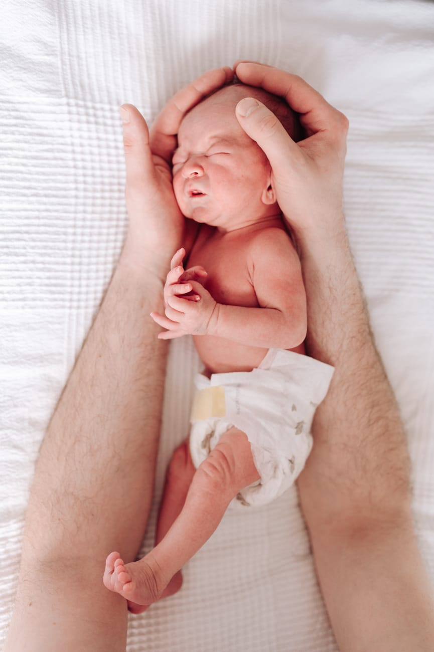 Prężący się noworodek między dłońmi taty sesja noworodkowa lifestyle Gdynia