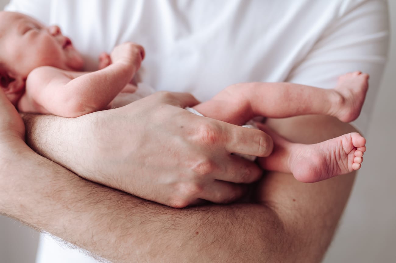 Dłoń taty otula noworodka detal sesja w domu Gdynia