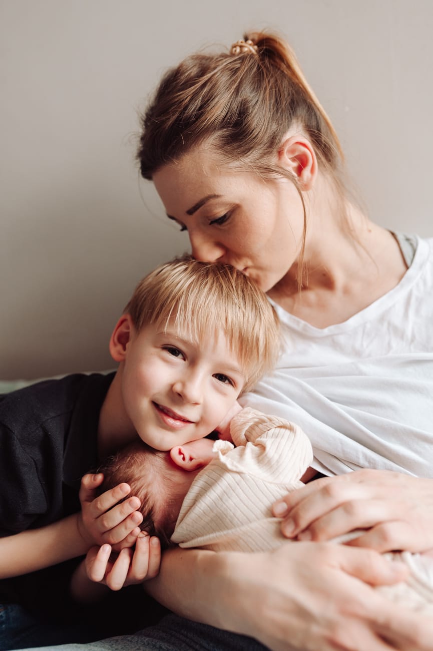 Mama z dwójką dzieci na łóżku sesja noworodkowa