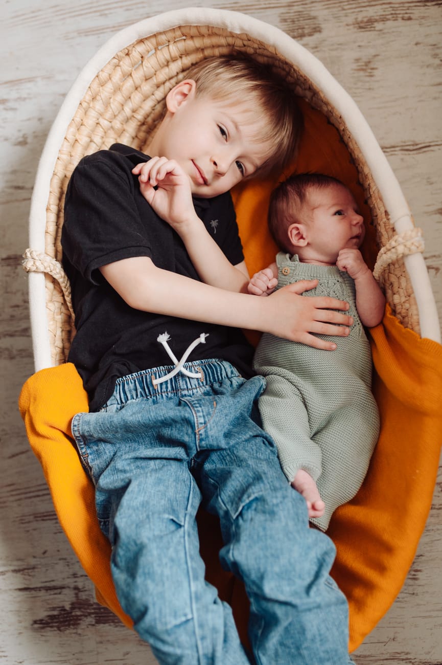 Starszy brat razem z noworodkiem leżą w koszu Mojżesza sesja noworodkowa lifestyle