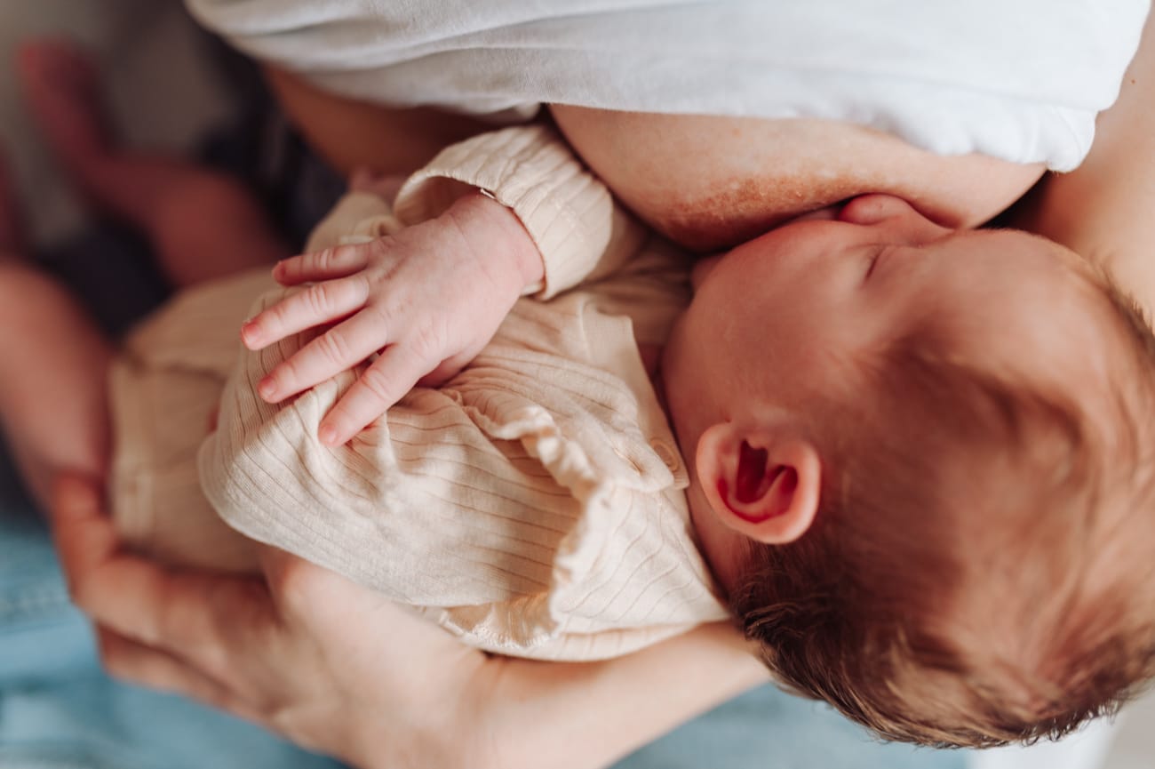 Mama karmiąca noworodka na łóżku sesja noworodkowa w domu
