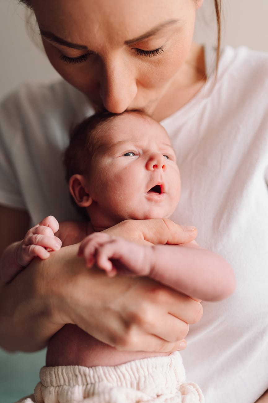 Mama całuje główkę noworodka sesja mama z dziećmi