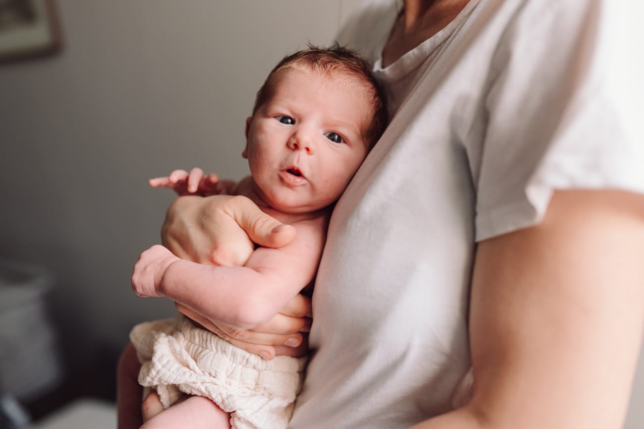 Noworodek w ramionach mamy patrzy w obiektyw sesja w domu