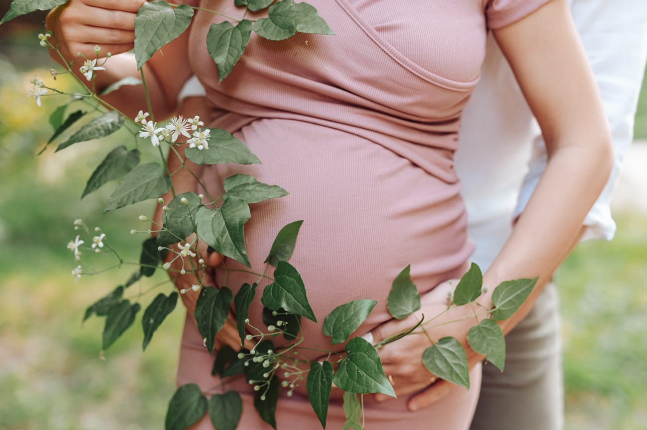 Zbliżenie na brzuszek ciążowy otulony dłońmi.