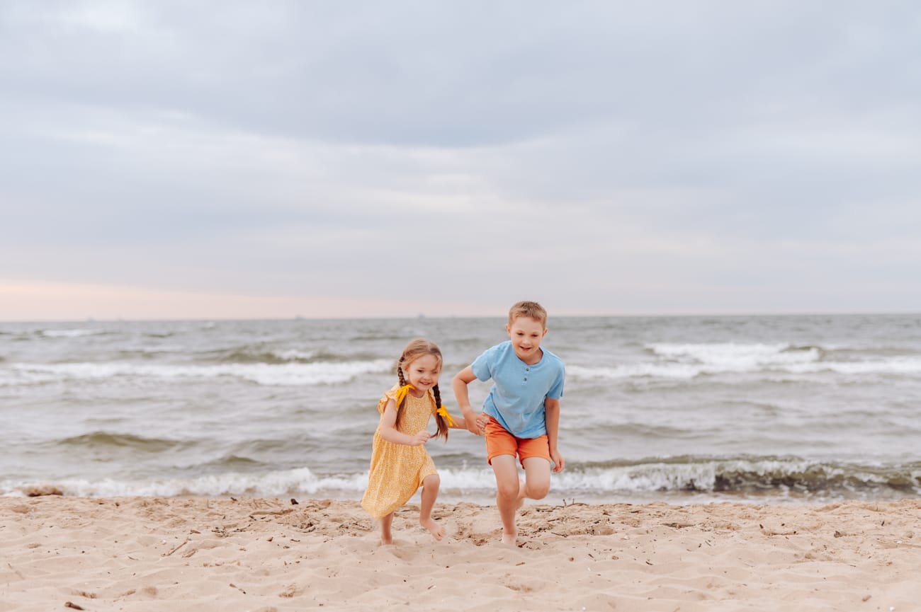 Dzieci biegną po plaży wzburzone morze w tle