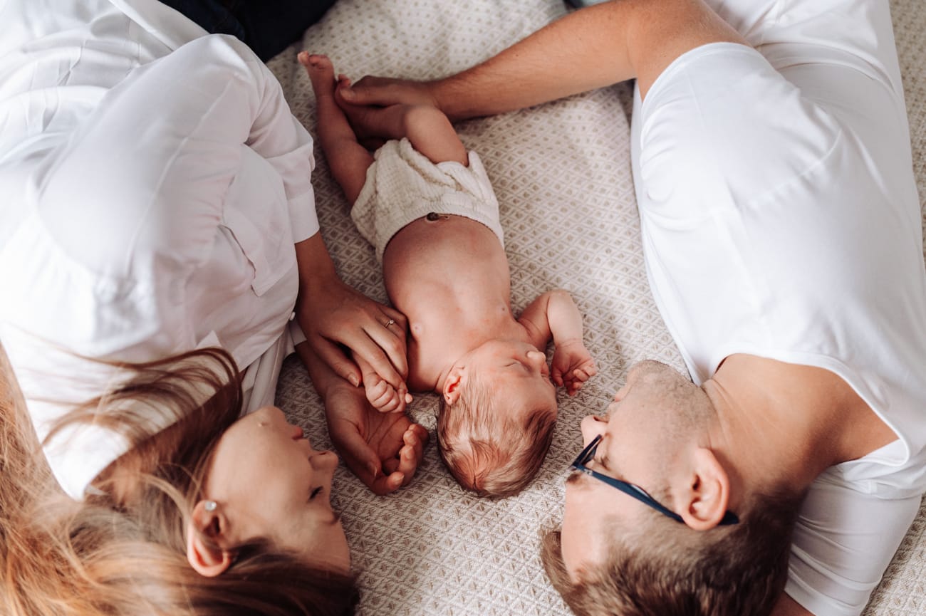 Rodzice z noworodkiem na łóżku domowa sesja Gdynia