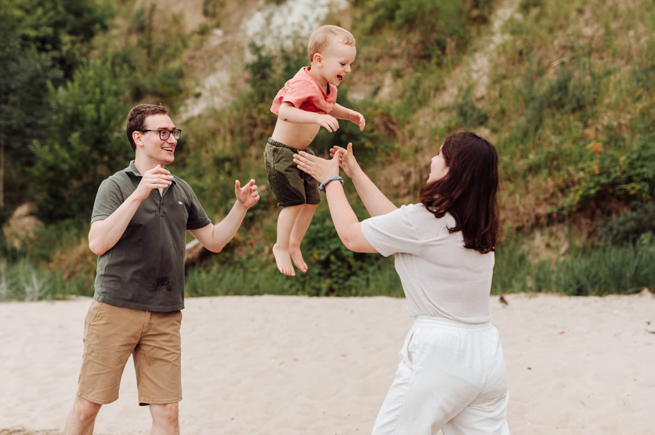 Rodzice bawią się z  dwulatkiem na plaży sesja rodzinna