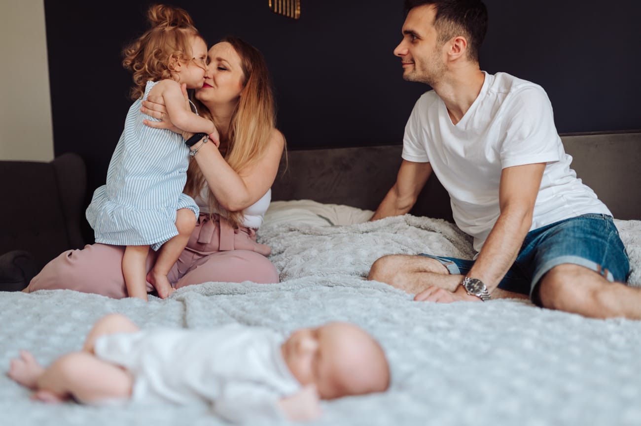 Rodzina bawi się w tle noworodek na łóżku sesja Gdańsk