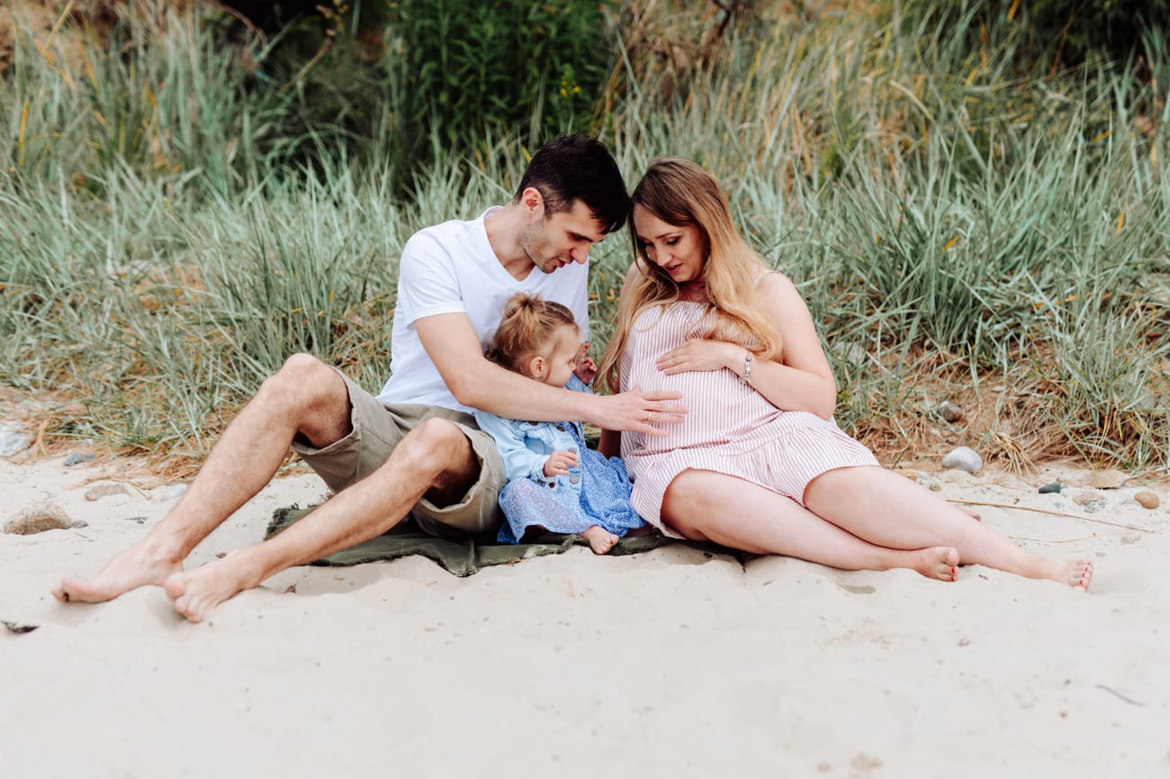 Rodzina na kocu na plaży sesja ciążowa ze starszym dzieckiem
