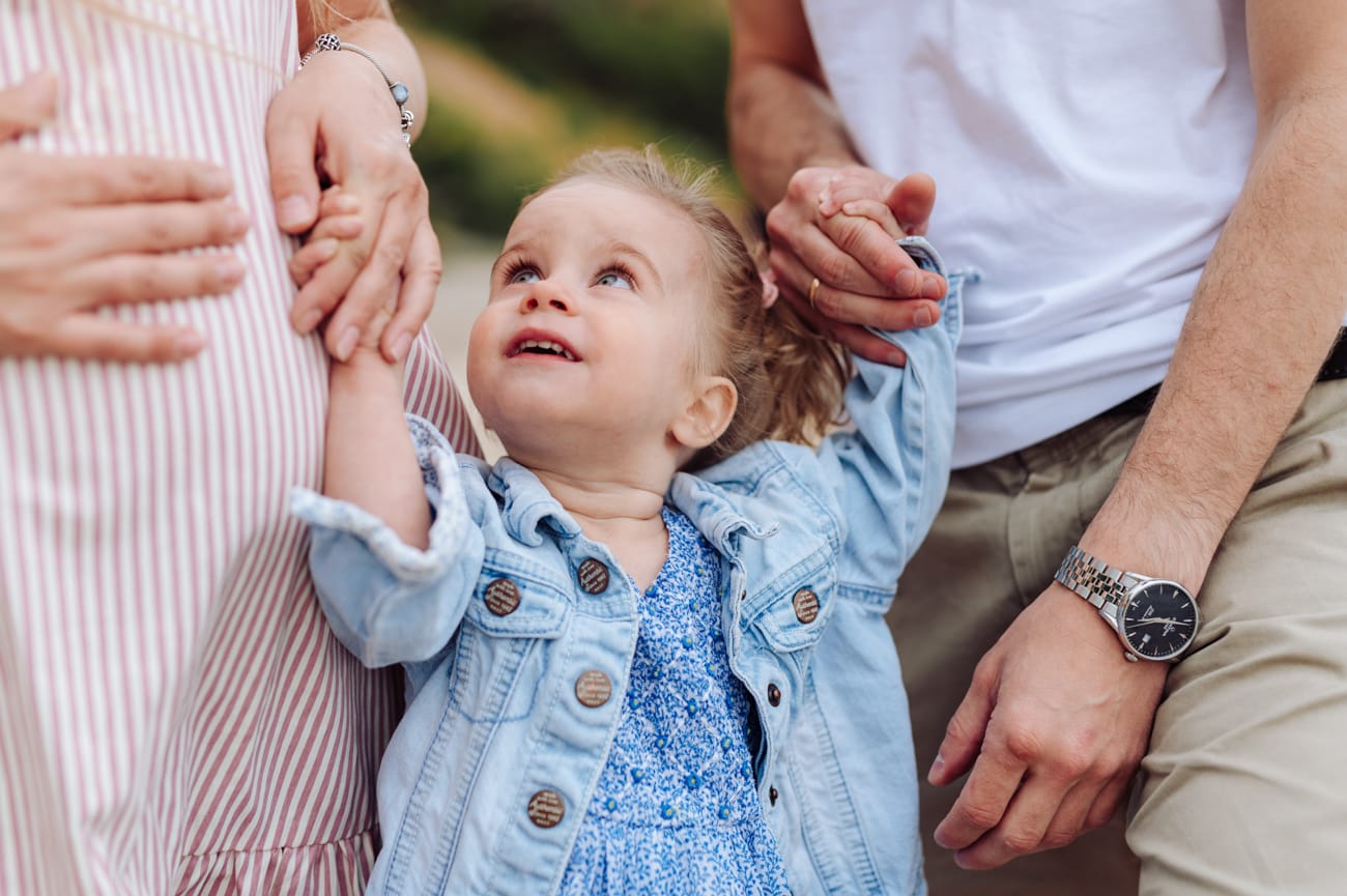 Dwulatka patrzy na mamę w ciąży sesja rodzinna nad morzem

