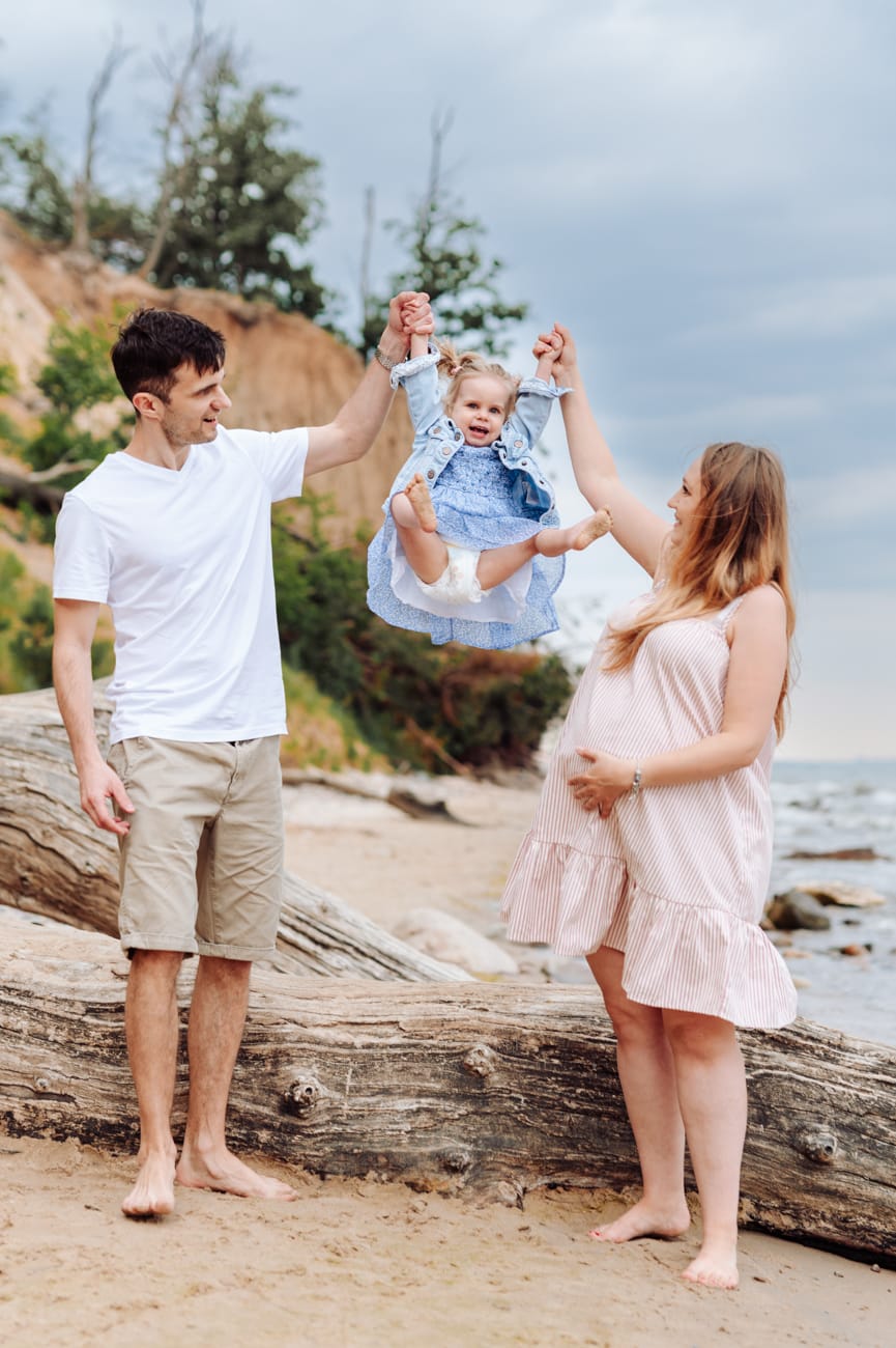 Rodzice huśtają córkę na plaży sesja ciążowa
