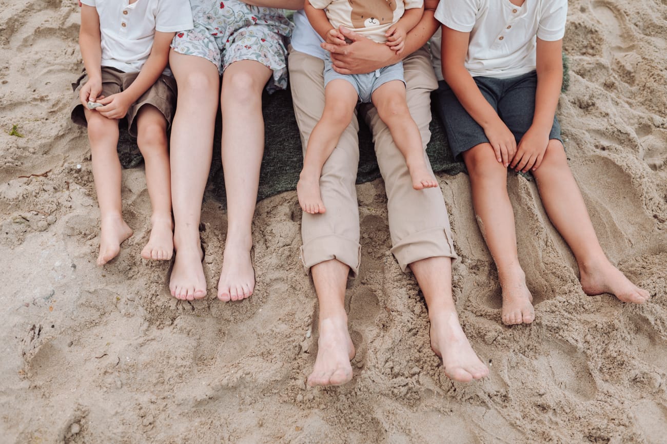 Zbliżenie na nogi rodziny wielodzietnej, która siedzi na nadmorskiej plaży.