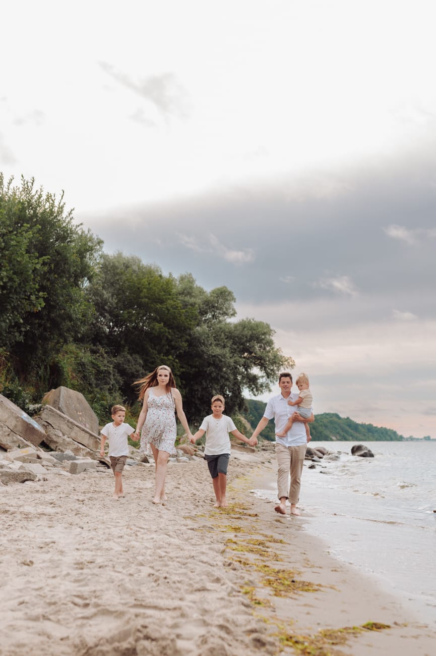 Rodzina podczas letniej sesji ciążowej nad morzem przy zachodzącym słońcu.