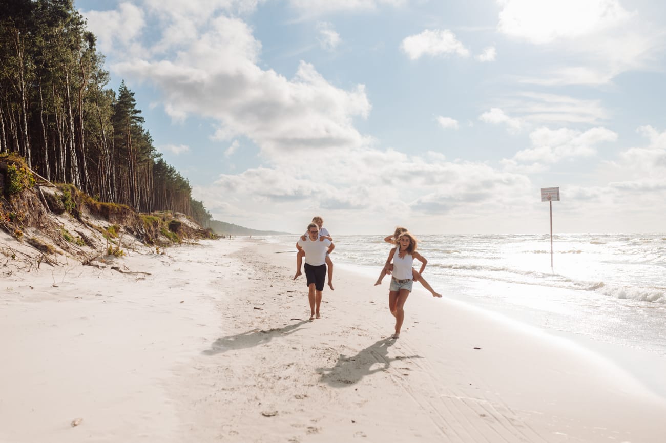 Rodzice biegnący brzegiem morza z dziećmi na barana sesja nad morzem