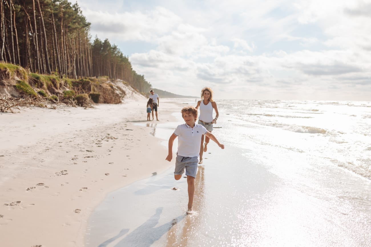 Chłopiec goniony przez rodzinę po plaży sesja rodzinna