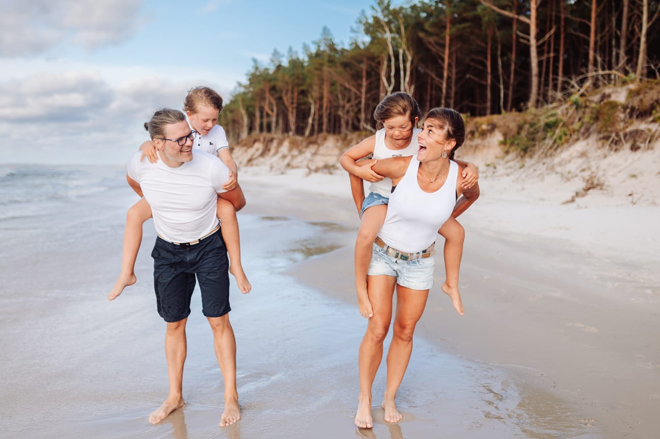 Dzieci na barana u rodziców na brzegu morza sesja rodzinna