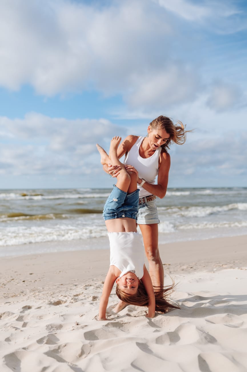 Córka stoi na rękach trzymana przez mamę sesja rodzinna nad morzem