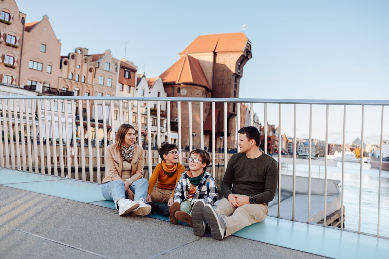 Rodzina z dwoma chłopcami siedzi na moście nad Motławą podczas rodzinnej sesji miejskiej.