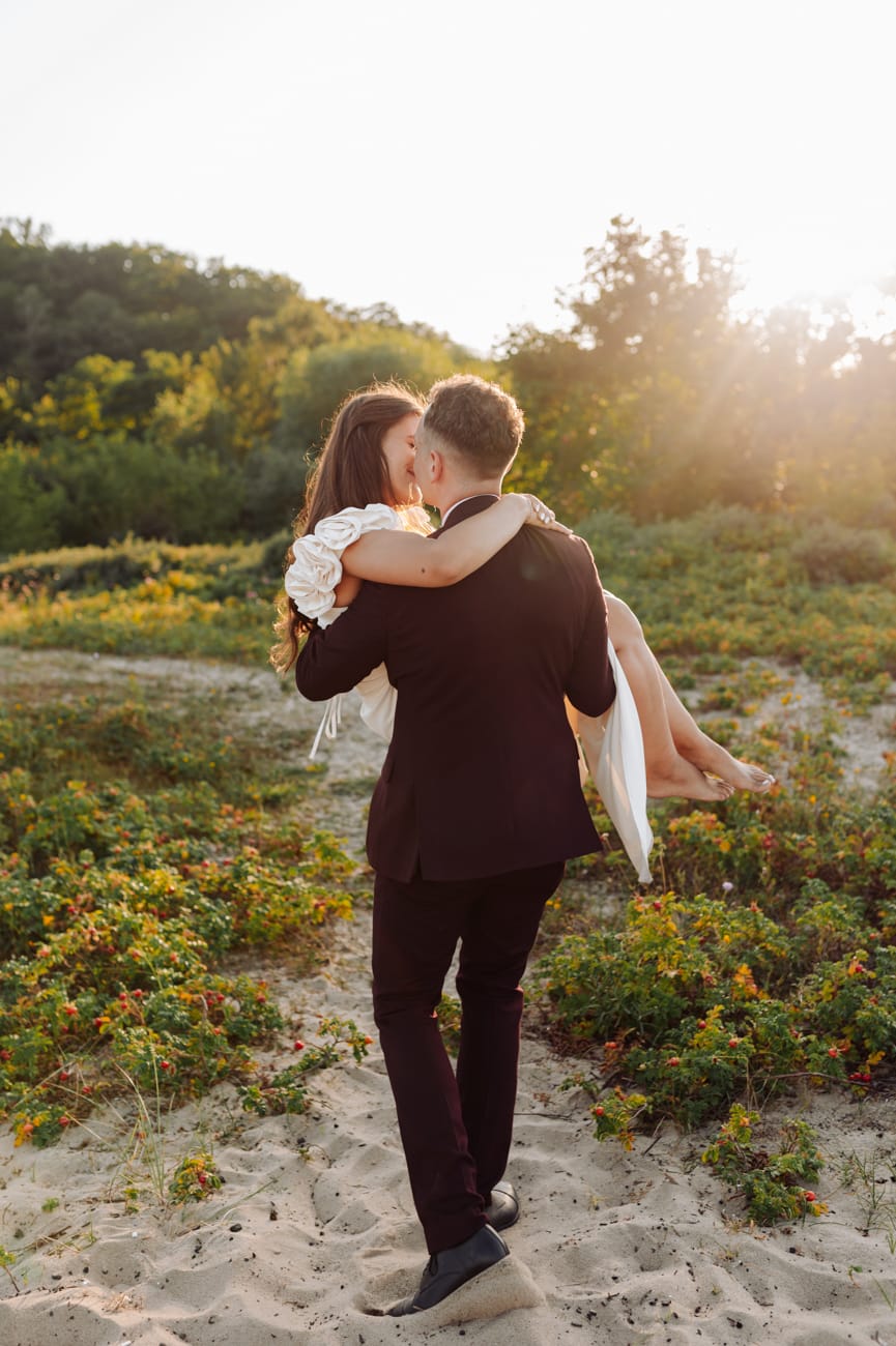 Pan młody ze swoją żoną na rękach łąka nad morzem Trójmiasto złota godzina
